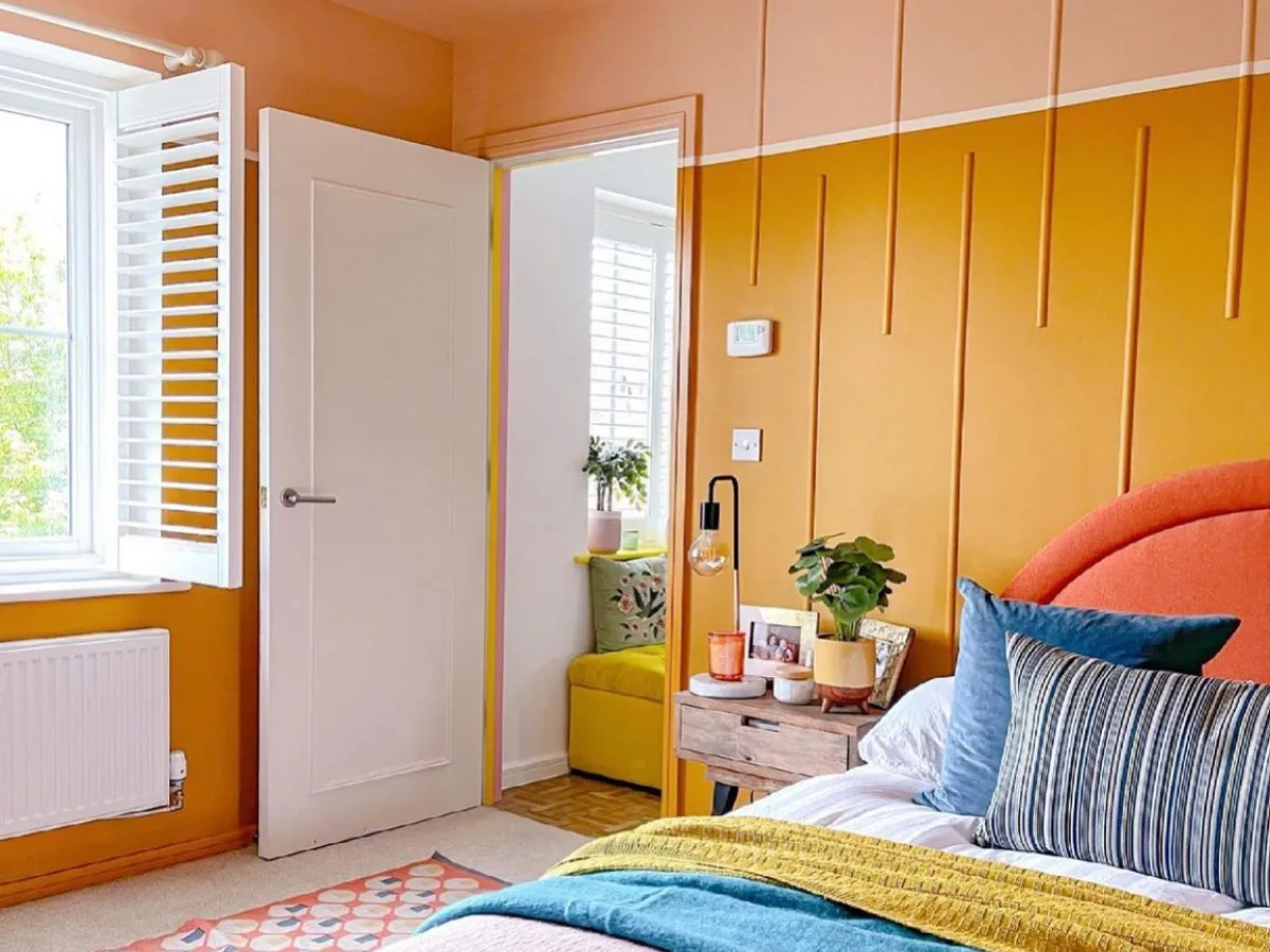 Colorful dopamine decor bedroom with mustard yellow paneled walls, a coral upholstered headboard, teal pillows, and vibrant patterned textiles.