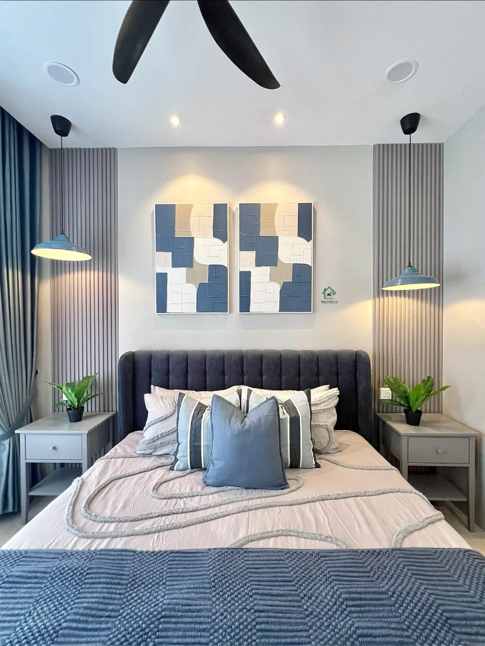 Modern bedroom with a charcoal upholstered headboard, blue curtains, gray fluted wall panels, and layered blue and white bedding