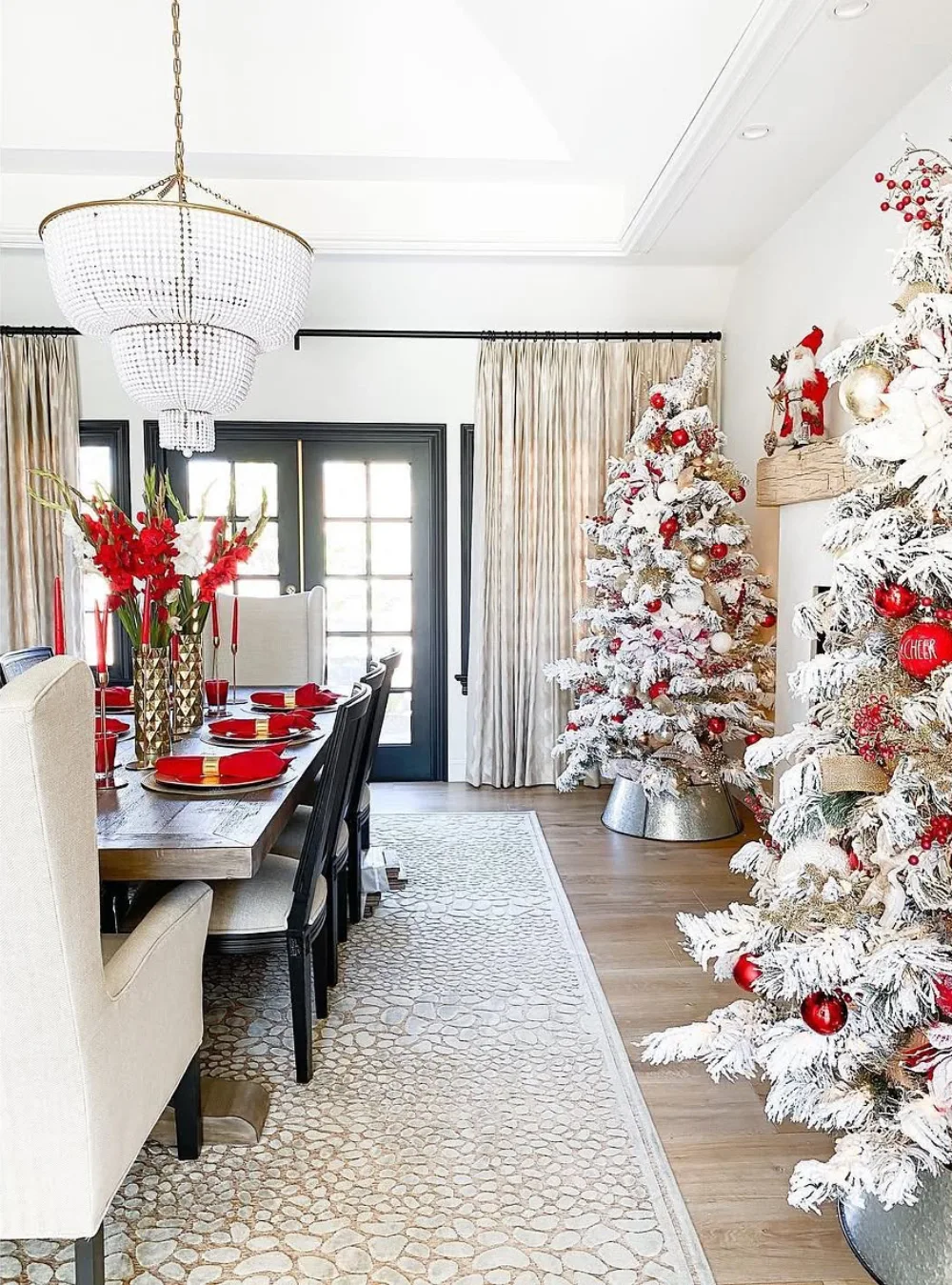 Elegant winter dining room with frosted Christmas trees, red accents, and a crystal chandelier