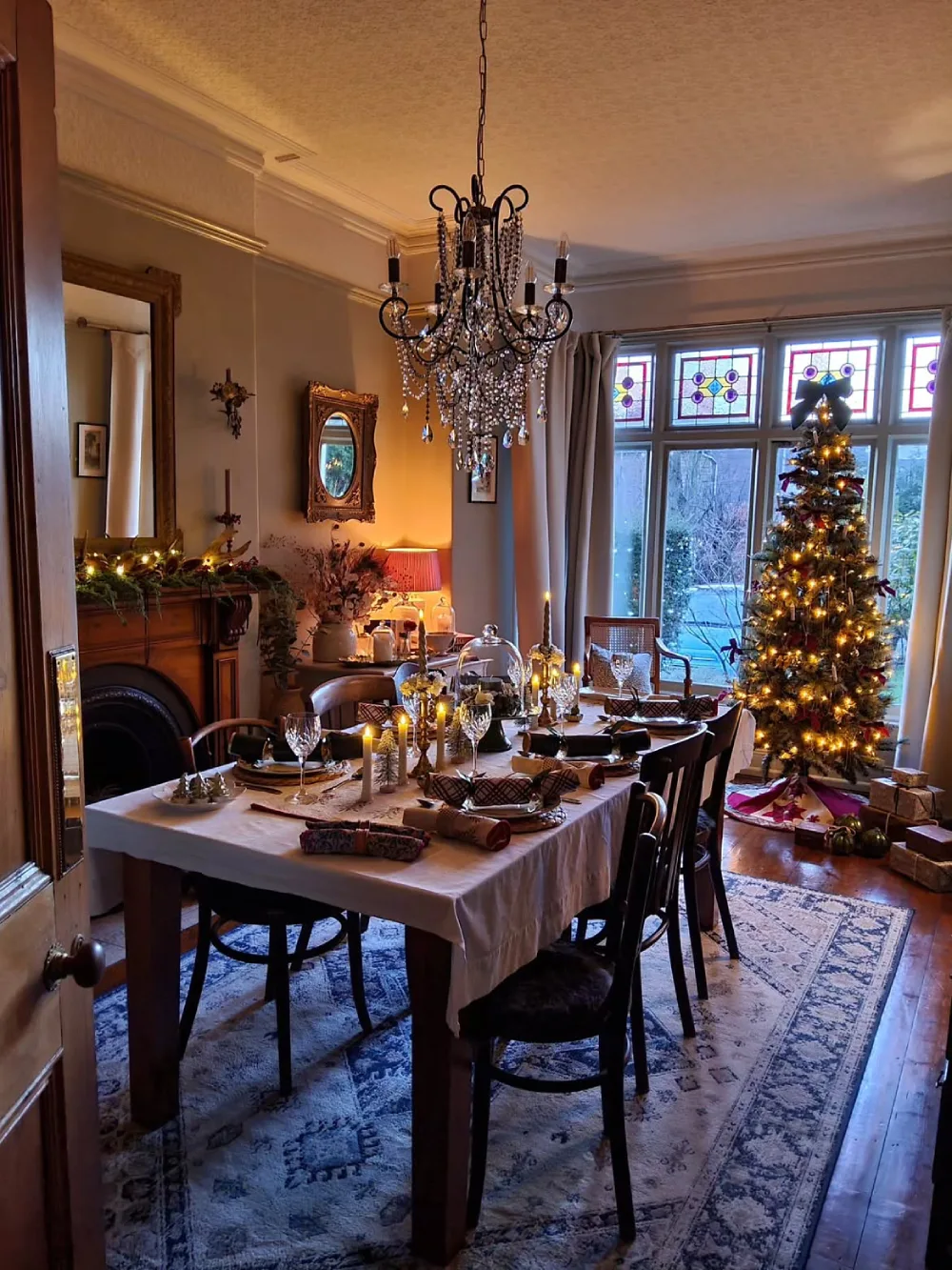 Winter dining room with a dark wood table, black chairs, Christmas greenery, candles, and a decorated tree