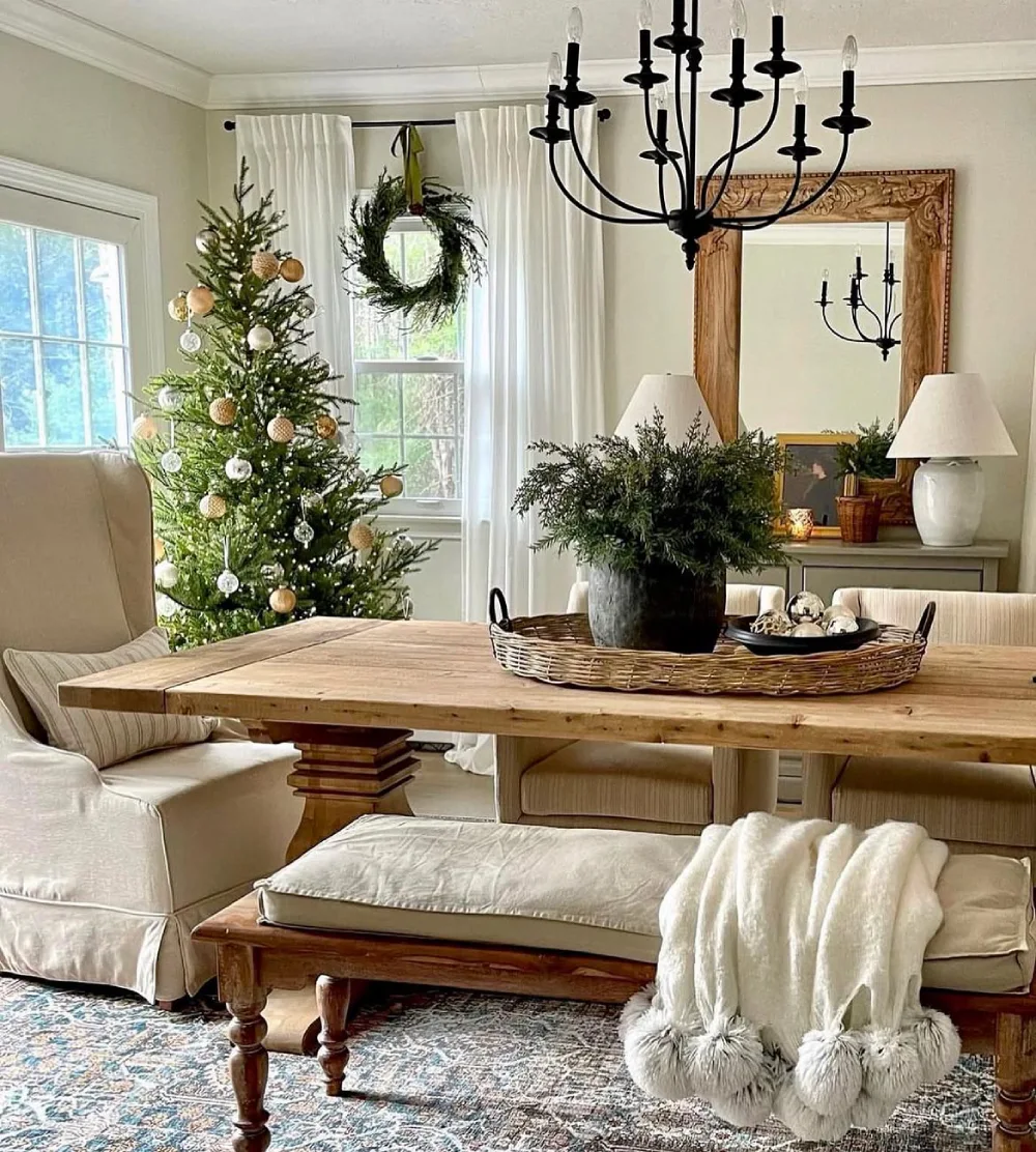 Cozy winter dining room with a rustic wood table, woven centerpiece tray, evergreen arrangement, and Christmas tree
