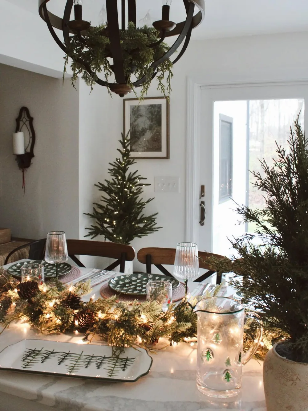Winter dining table decorated with evergreen garland, pinecones, string lights, and candlelit place settings