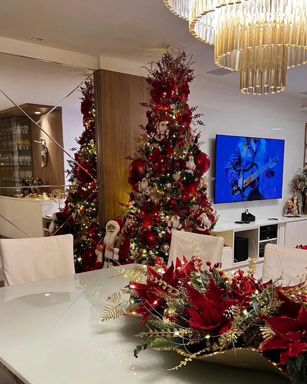 Glamorous winter dining room with a large red Christmas tree, red and gold centerpiece, and white dining chairs