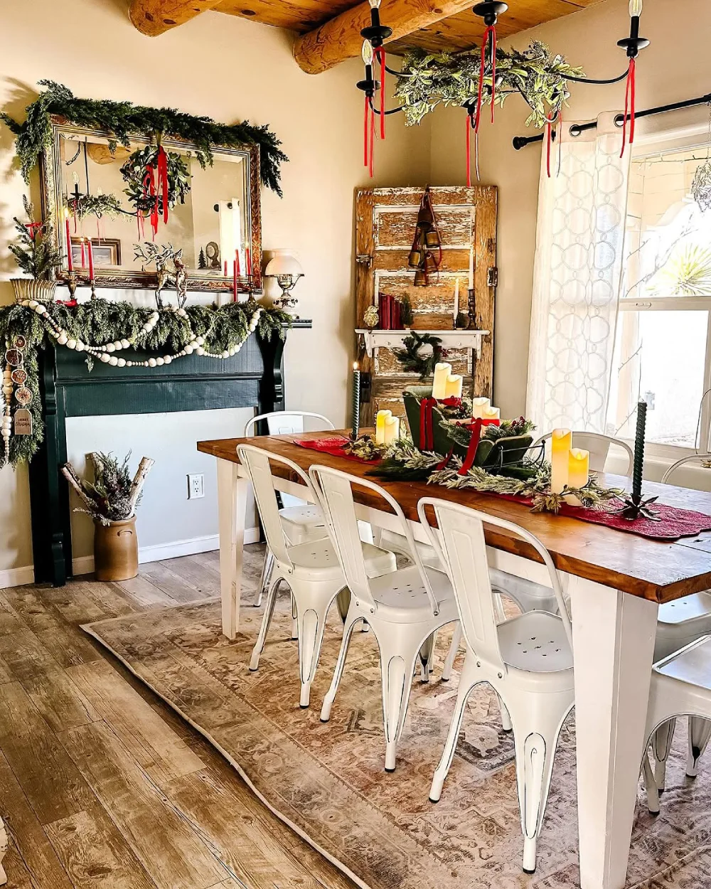 Rustic winter dining room with evergreen garlands, candles, red ribbons, and a wooden dining table