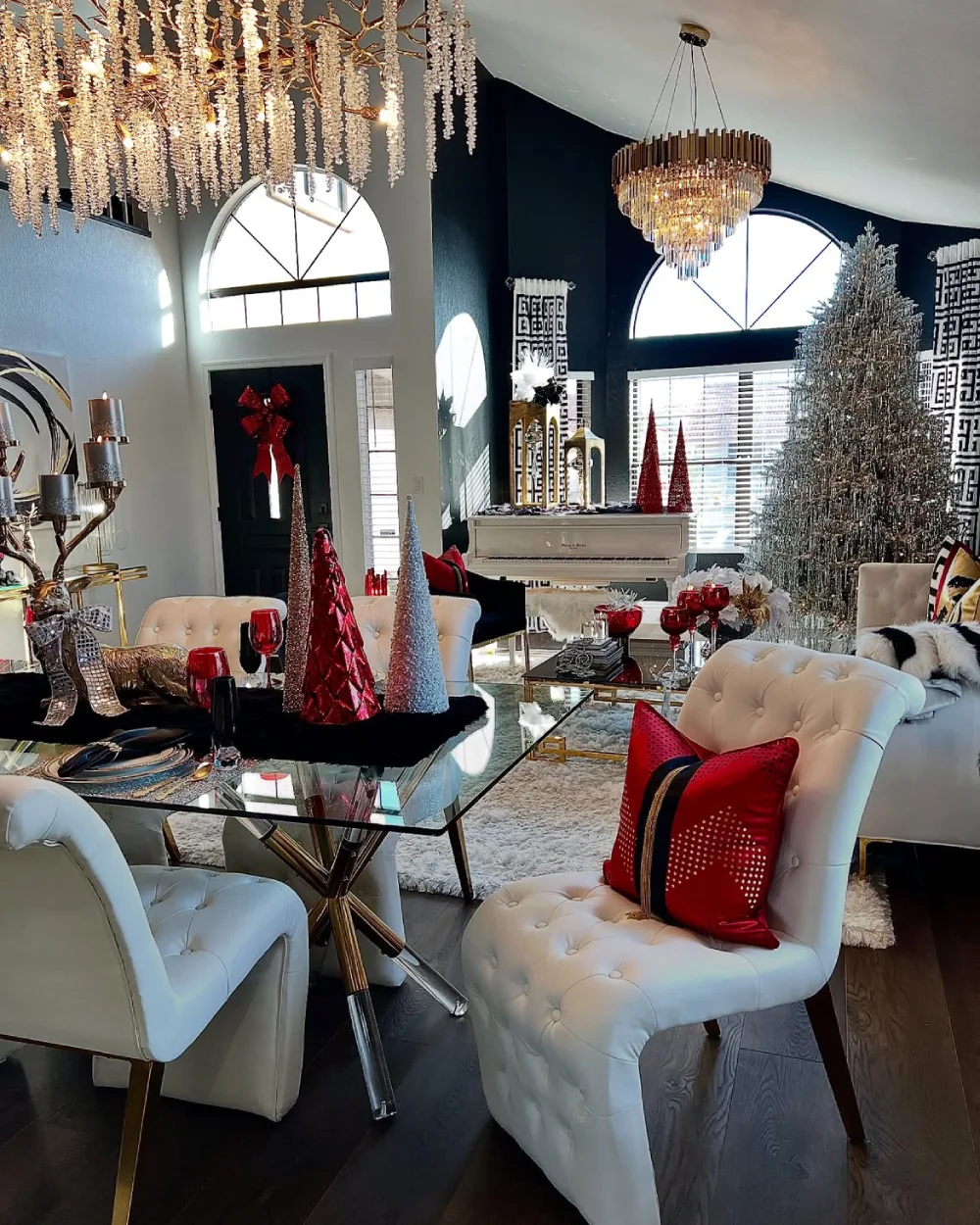 Glamorous winter dining room with white chairs, red decorations, silver Christmas trees, and crystal chandeliers