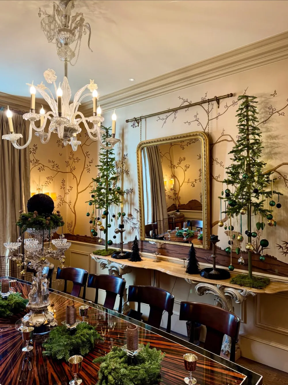 Vintage-inspired winter dining room with evergreen trees, ornate mirror, candles, and dark wood furniture