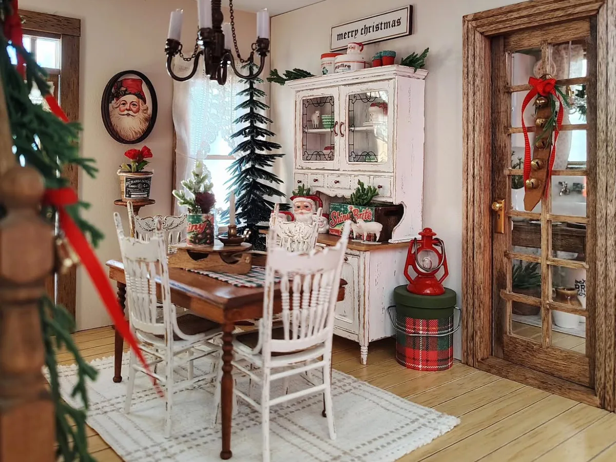Cozy winter dining room with a rustic wooden table, white chairs, vintage cabinet, Christmas decorations, and warm seasonal accents.