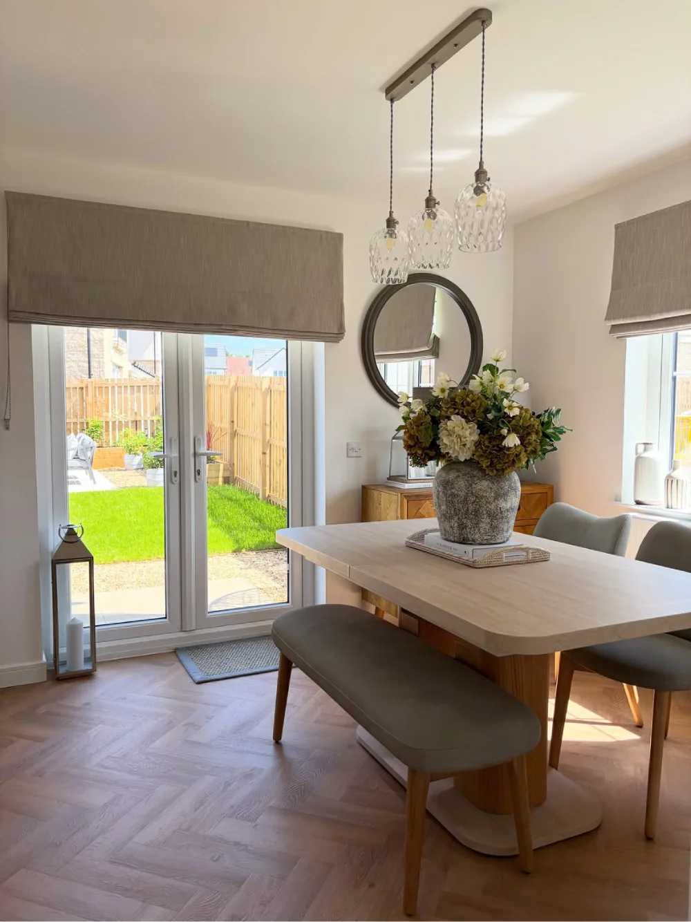 Bright open dining room with a wood table, upholstered bench, glass doors, and garden views