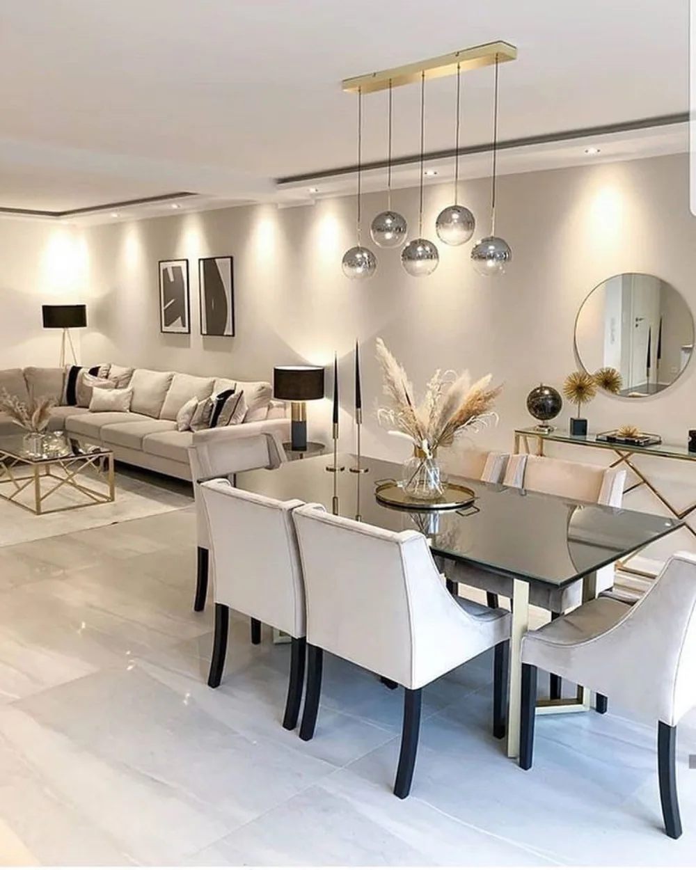 White open-concept dining and living room with a glass table, upholstered chairs, and silver pendant lights
