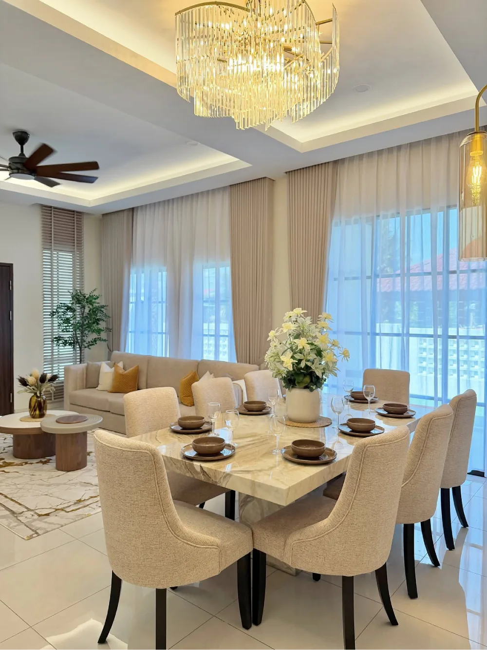 Elegant dining room with a marble table, cream chairs, large windows, and a statement crystal chandelier