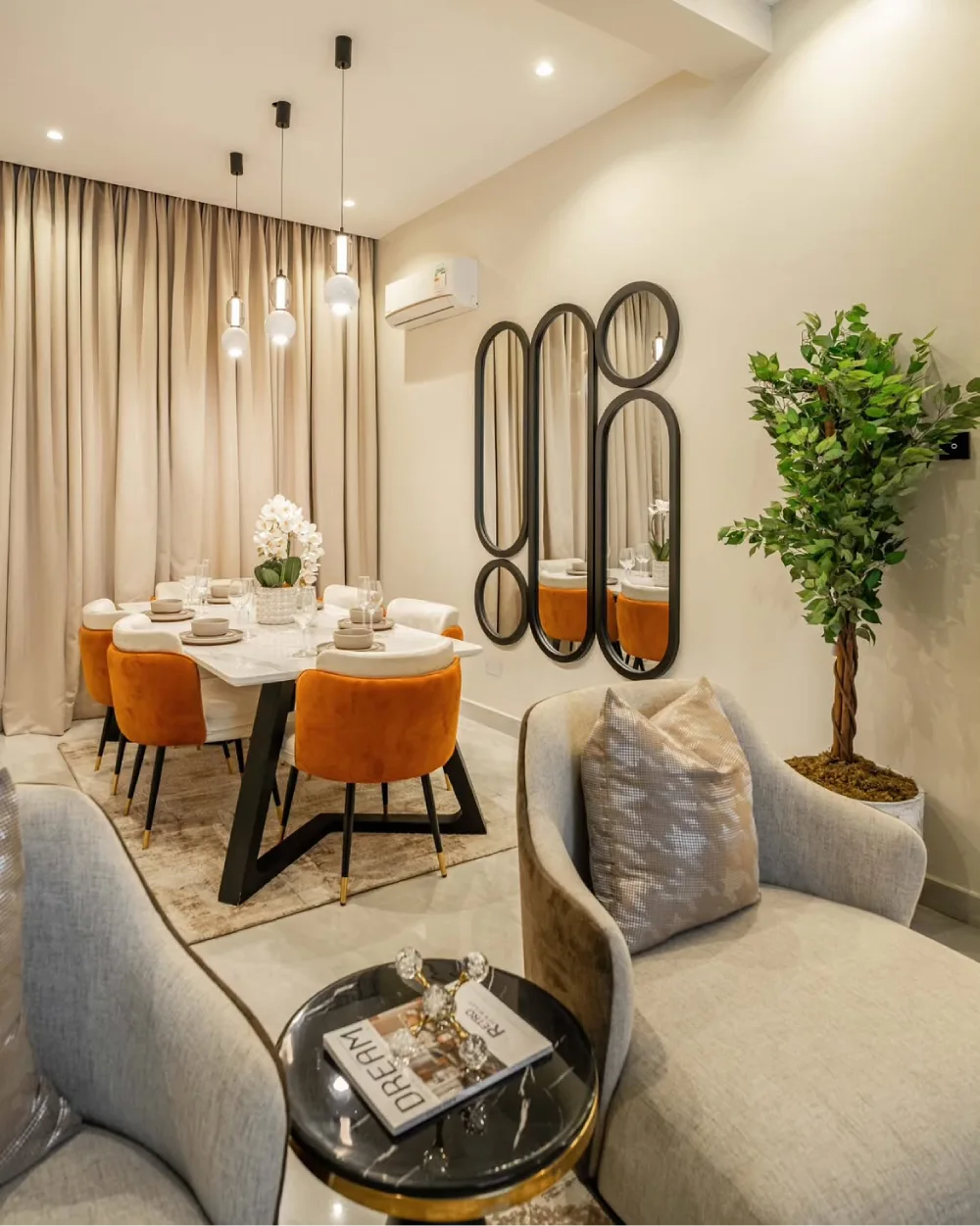 Elegant dining room with orange upholstered chairs, a white table, globe pendant lights, and decorative wall mirrors