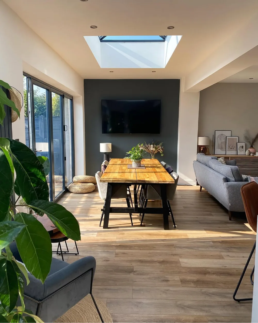 Open dining room with a wood table beneath a skylight and large glass doors beside the living area