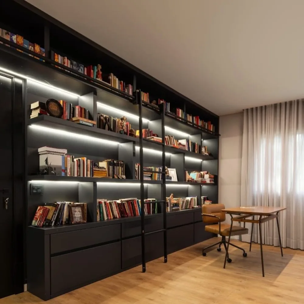 dark built-in bookshelf with books and accent lighting in a home office
