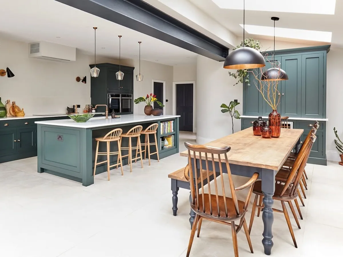 Open-concept kitchen with deep blue-green cabinets, a large island, wood dining table, and skylights connecting the kitchen and dining area.