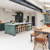 Open-concept kitchen with deep blue-green cabinets, a large island, wood dining table, and skylights connecting the kitchen and dining area.