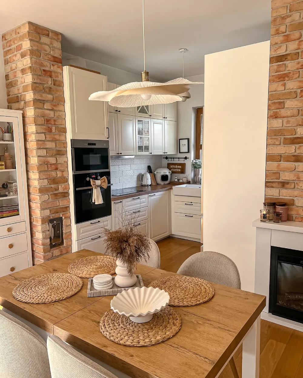 Small cream kitchen framed by exposed brick walls and a wood dining table
