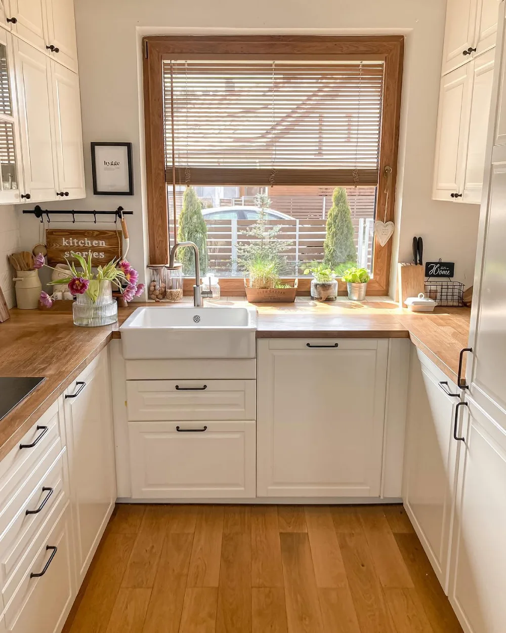 Small white kitchen with a farmhouse sink beneath a large wood-framed window
