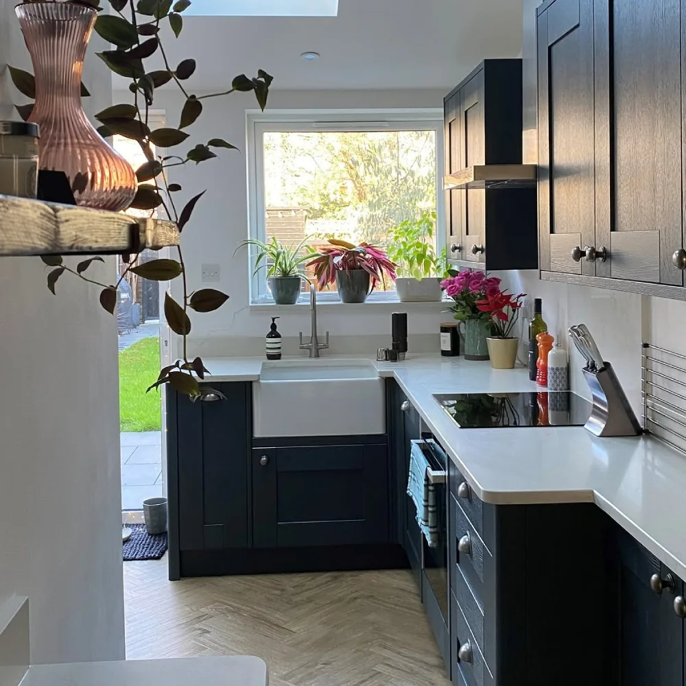 navy and white kitchen with farmhouse sink, white counters, and garden view