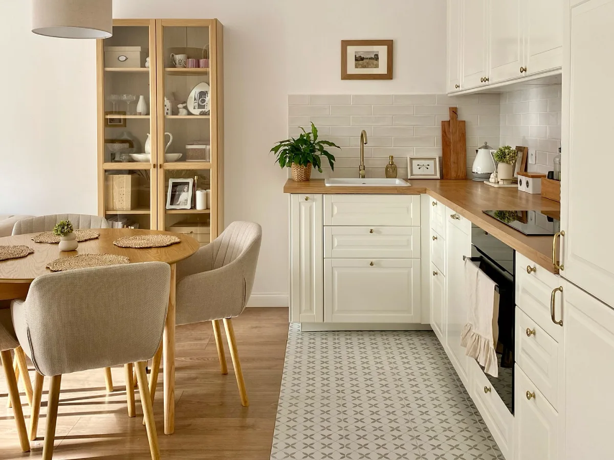 Small white kitchen with wood countertops, glass-front cabinet, dining table, and patterned floor tile