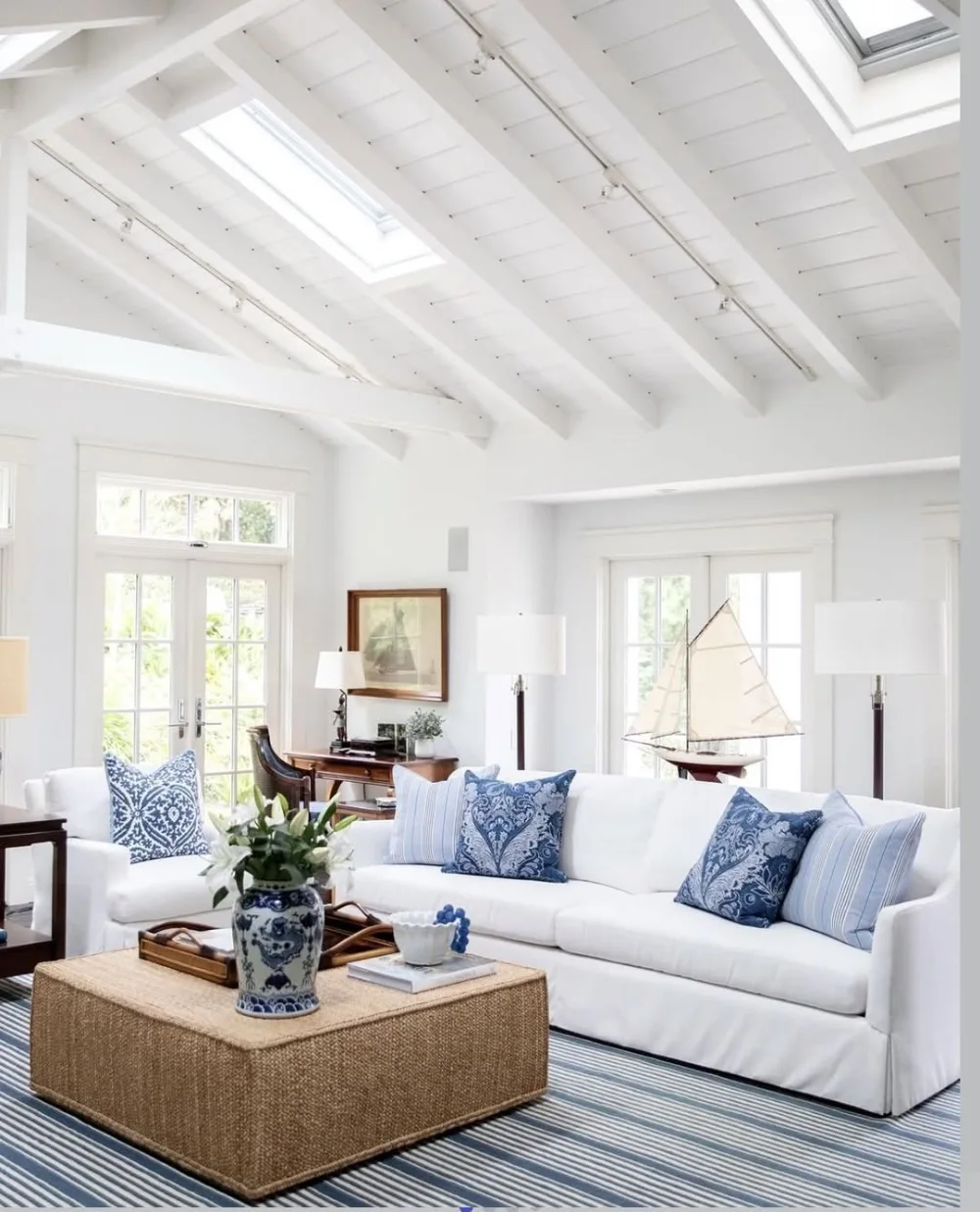 Bright coastal living room with white sofa, blue patterned pillows, striped rug, and skylights