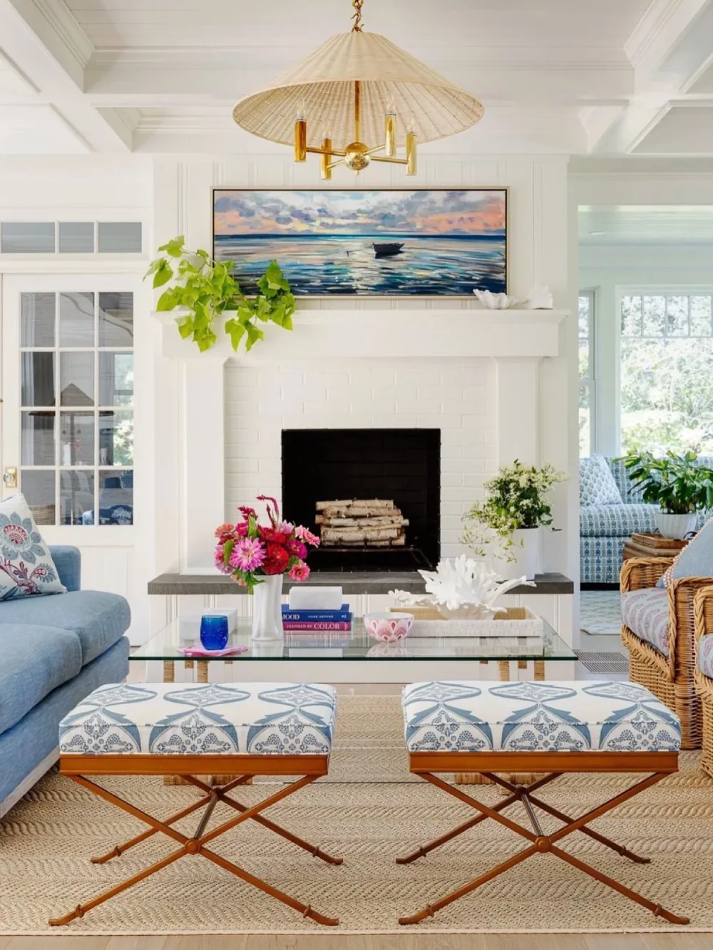 Coastal living room with blue seating, nautical artwork, woven ottoman, and a white fireplace