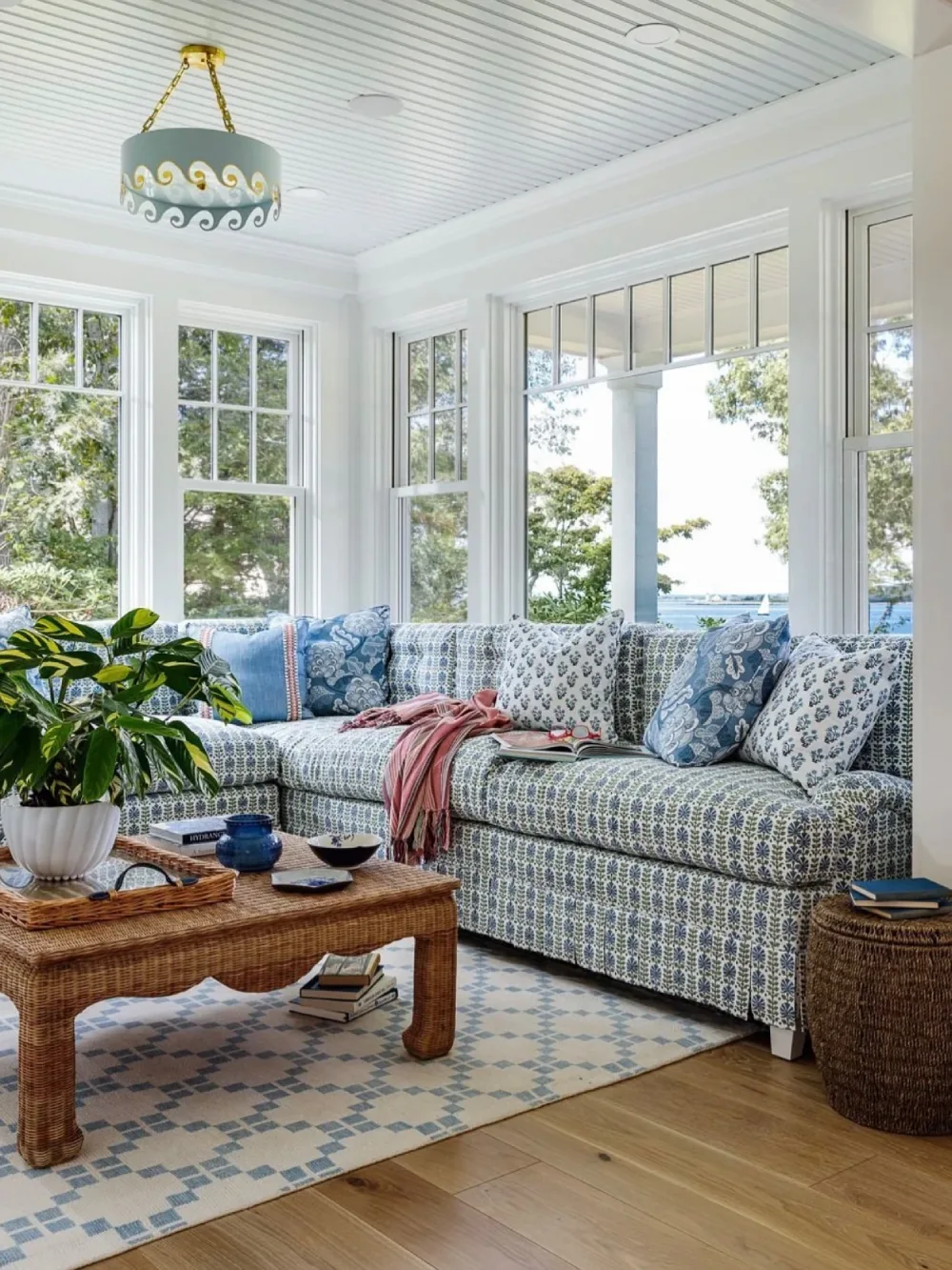 Bright coastal living room with blue patterned sectional sofa, wicker coffee table, and large windows