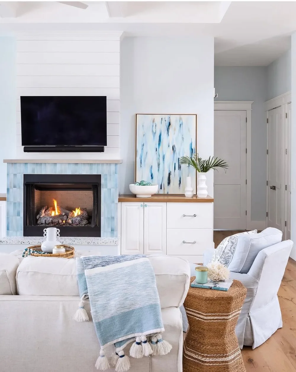 Coastal living room with white seating, pale blue accents, woven side table, and blue fireplace tile