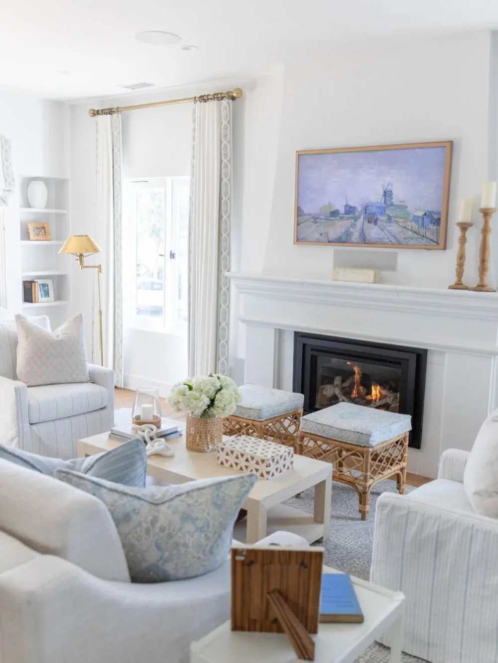 Light coastal living room with white seating, blue accents, woven ottomans, and a fireplace