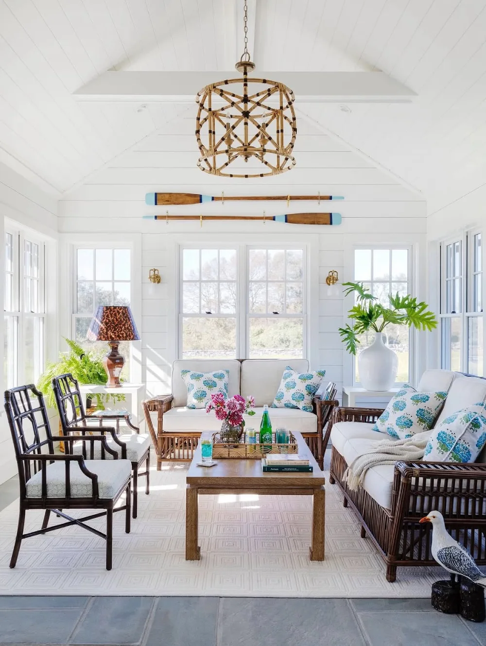 Bright coastal living room with wicker furniture, blue patterned pillows, white walls, and nautical decor