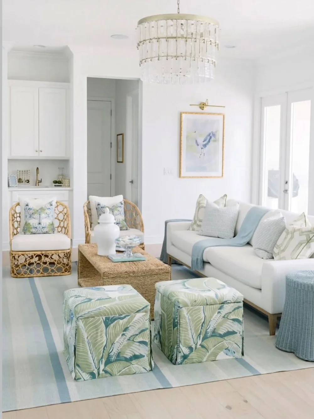 Light coastal living room with white sofa, pale blue textiles, woven coffee table, and green patterned ottomans
