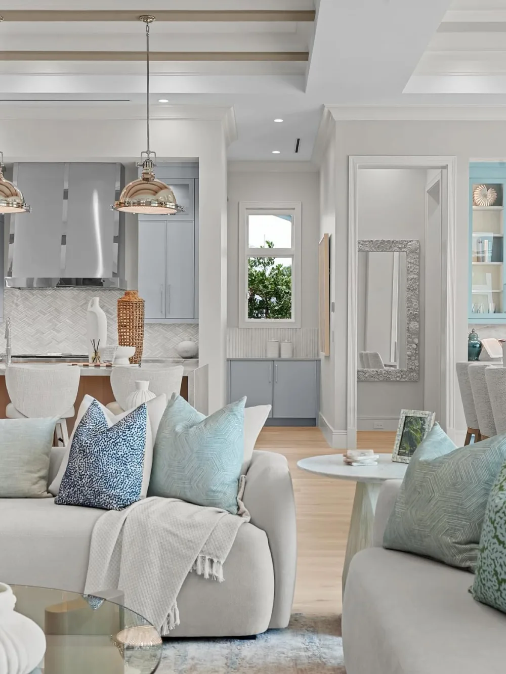 Coastal living room with white sofas, pale blue pillows, natural wood, and neutral decor
