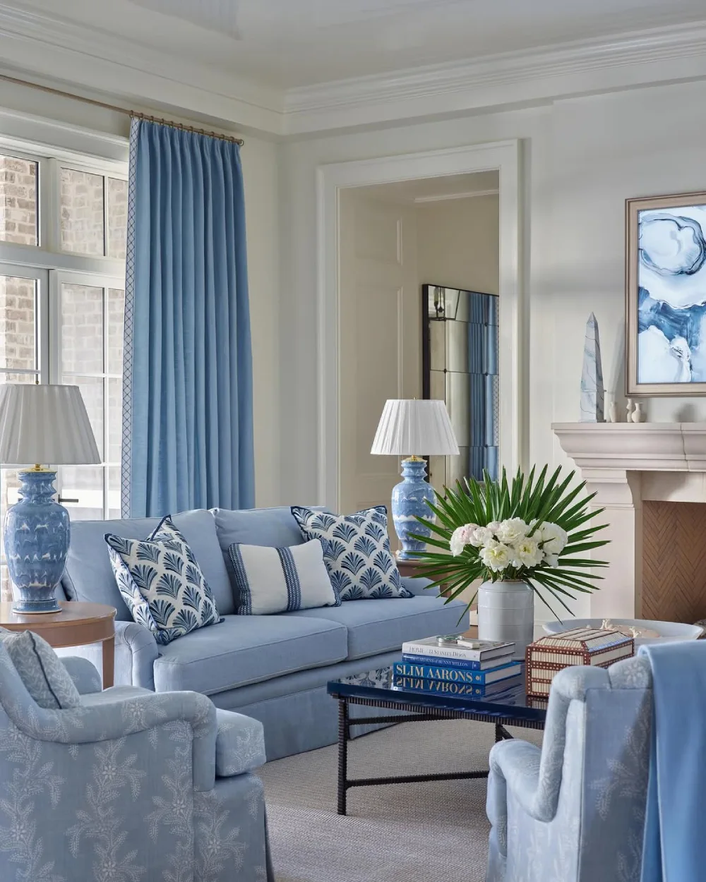 Elegant coastal living room with blue curtains, pale blue sofa, patterned pillows, and natural accents