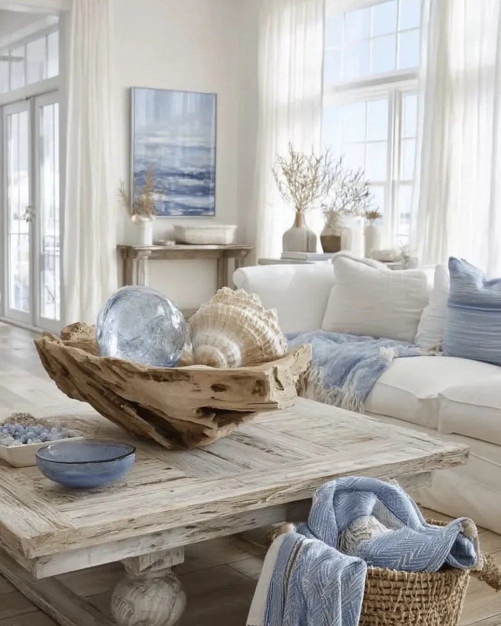 Light coastal living room with white sofa, weathered wood coffee table, seashell decor, and blue accents