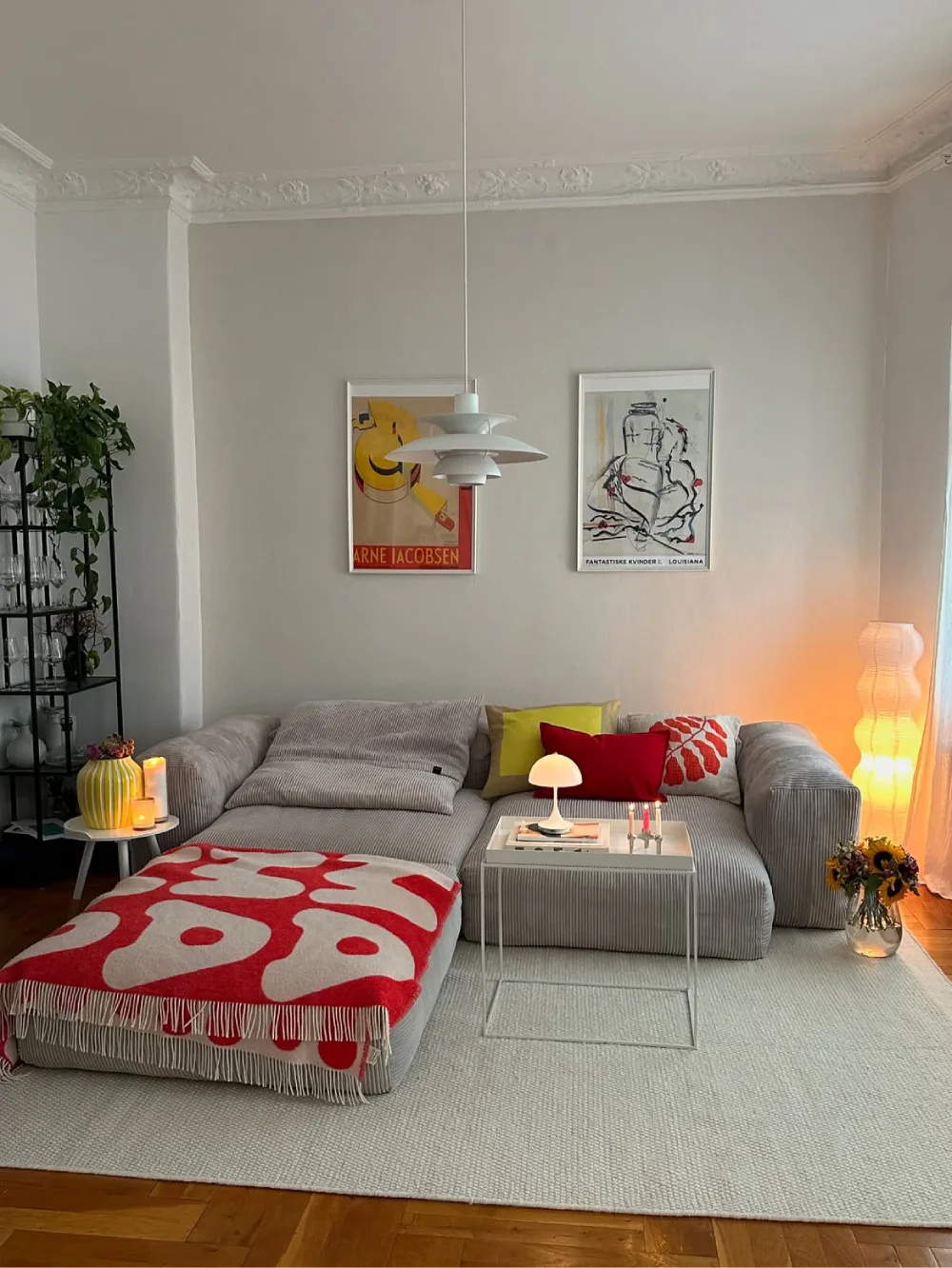 Light gray sectional with red pillows, a bold patterned throw, and colorful decor
