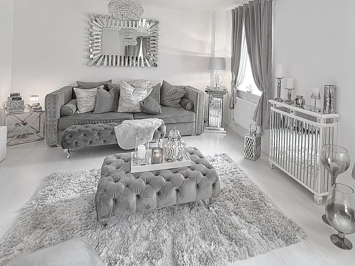 Elegant gray tufted sofa with layered pillows, a tufted ottoman, crystal chandeliers, and soft gray curtains in a neutral living room.