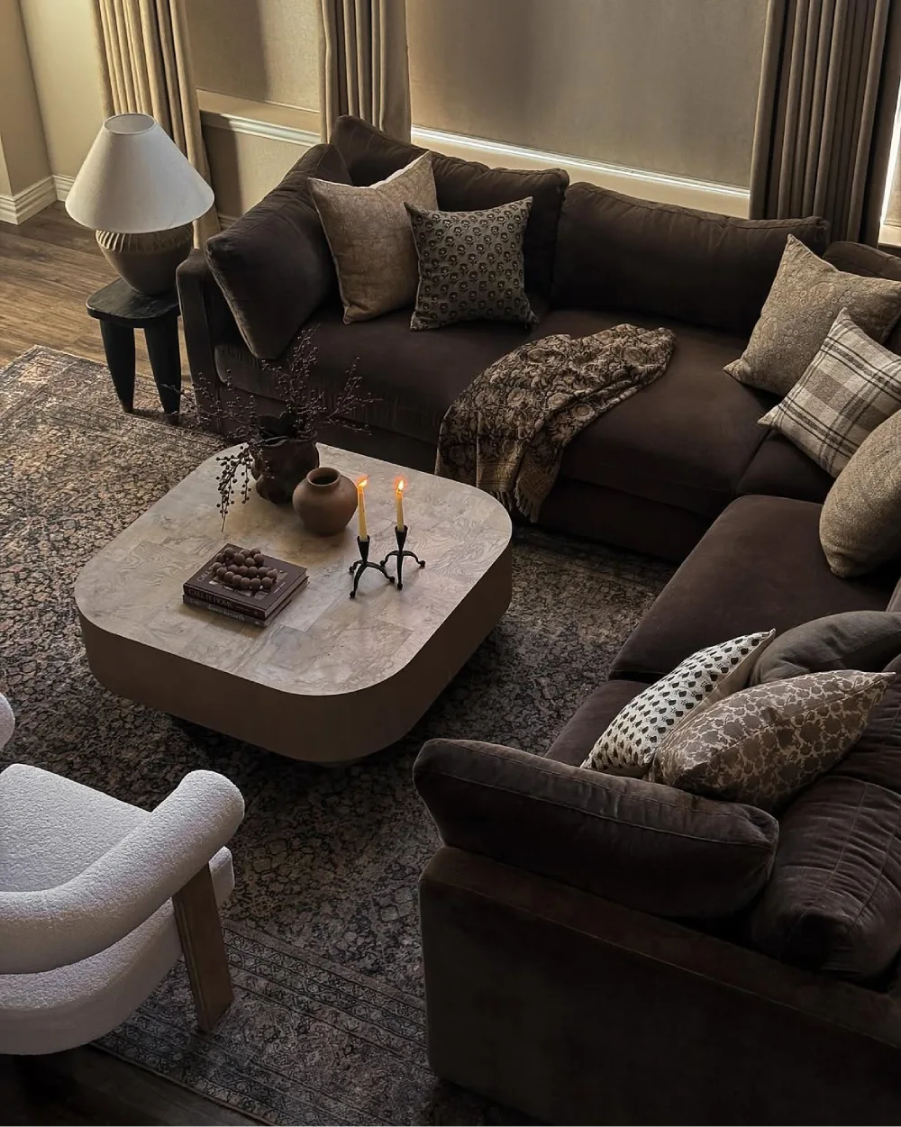 Dark brown sectional with patterned pillows, textured throw, and warm layered lighting