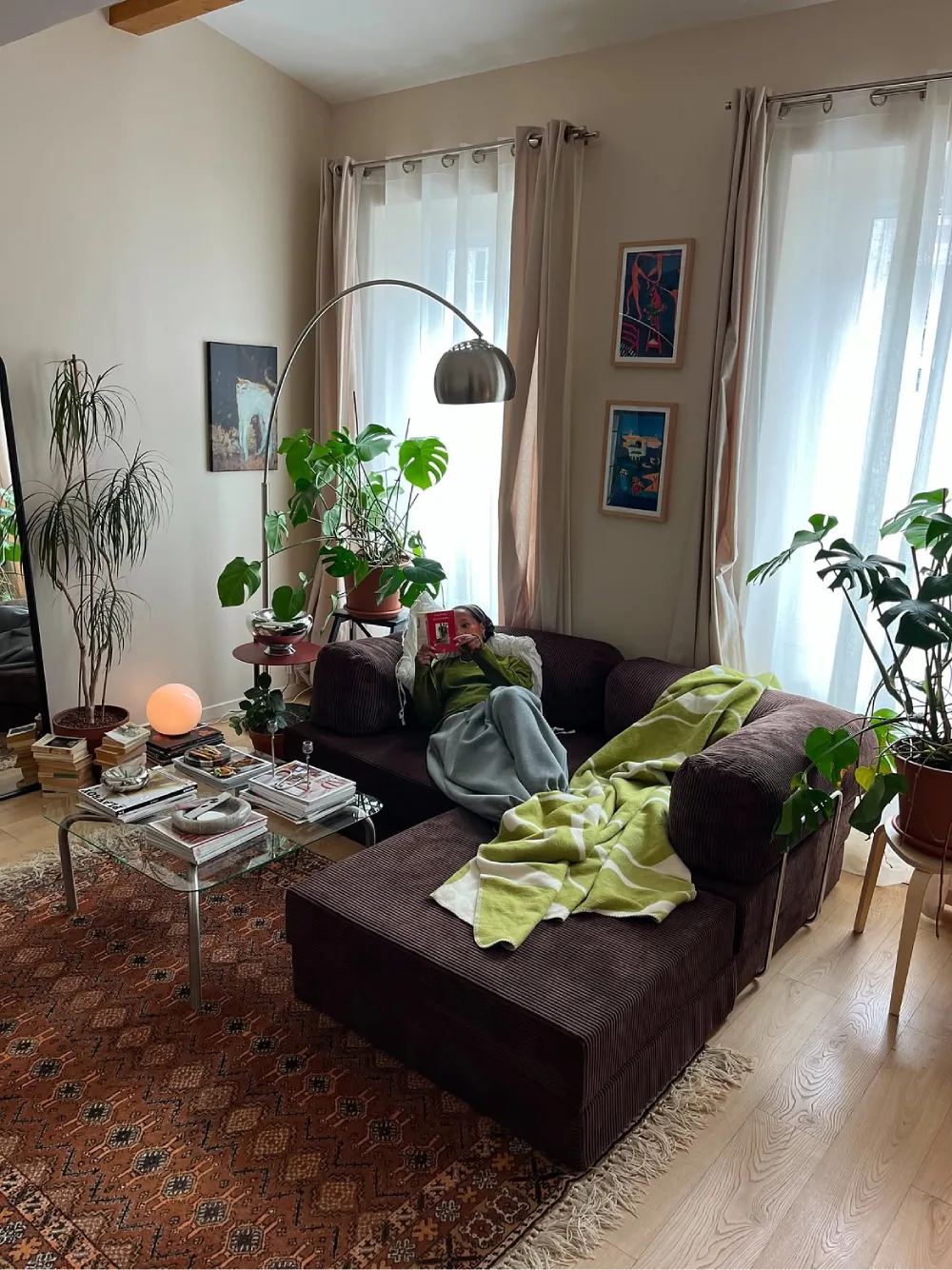 Dark brown sectional surrounded by houseplants, a patterned rug, and colorful accents