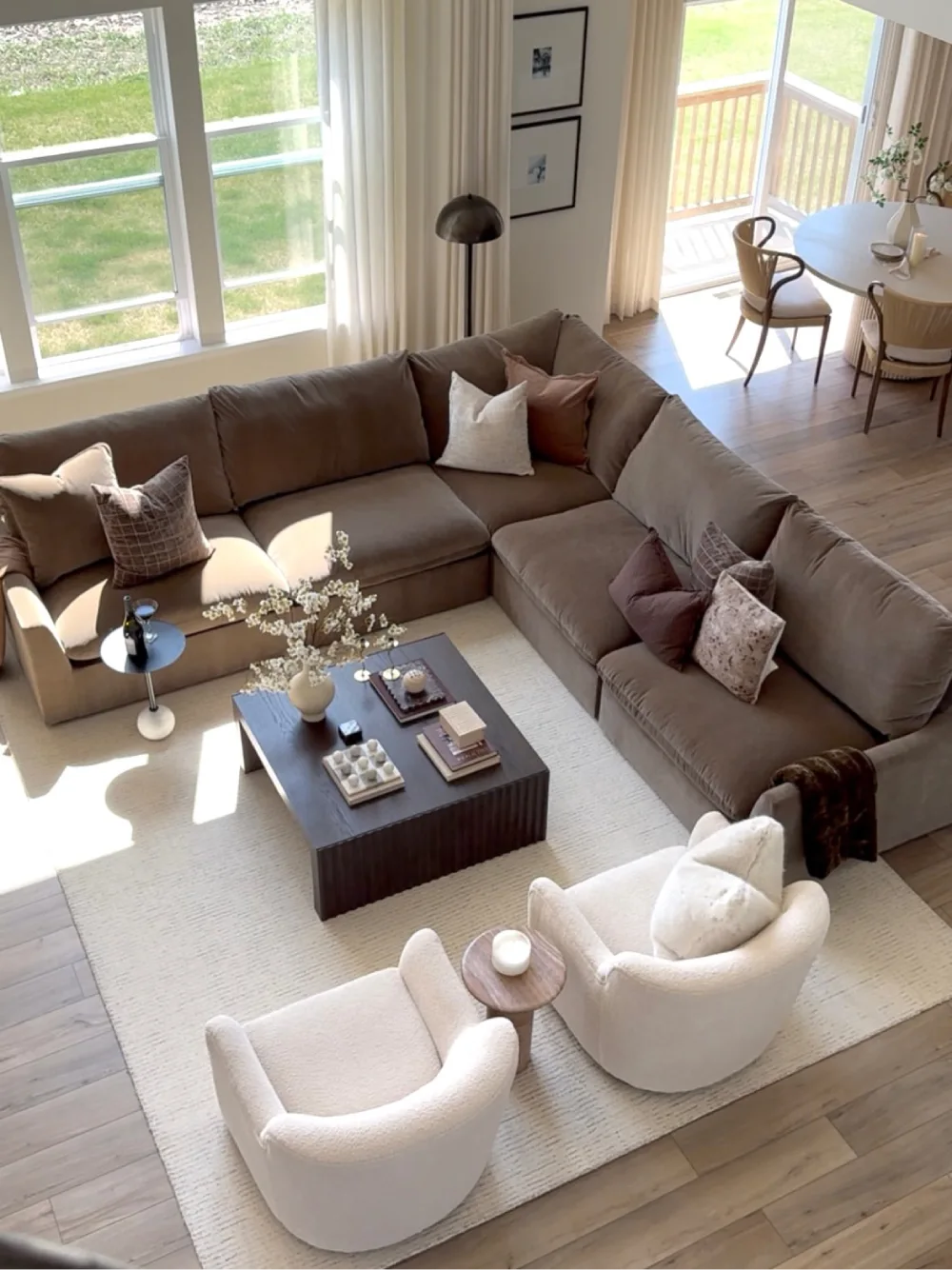 Taupe brown sectional with cream chairs, neutral rug, and large windows