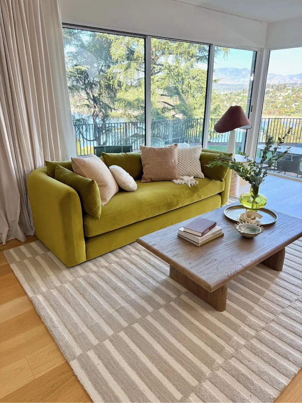 Olive green sofa with neutral pillows and a wooden coffee table in a bright living room