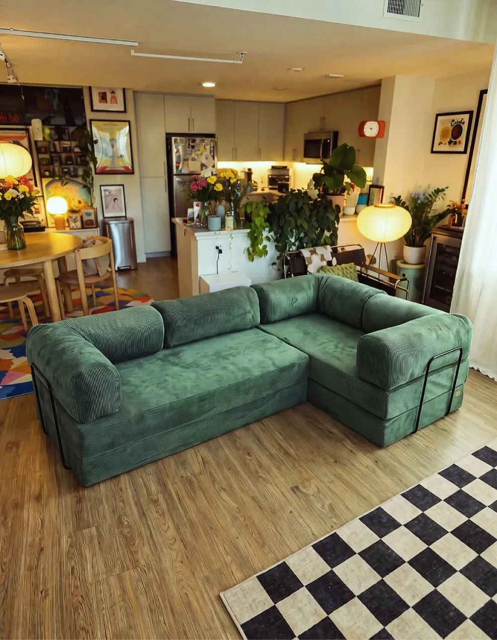 Soft green sectional sofa in a cozy open-plan living room with plants and artwork