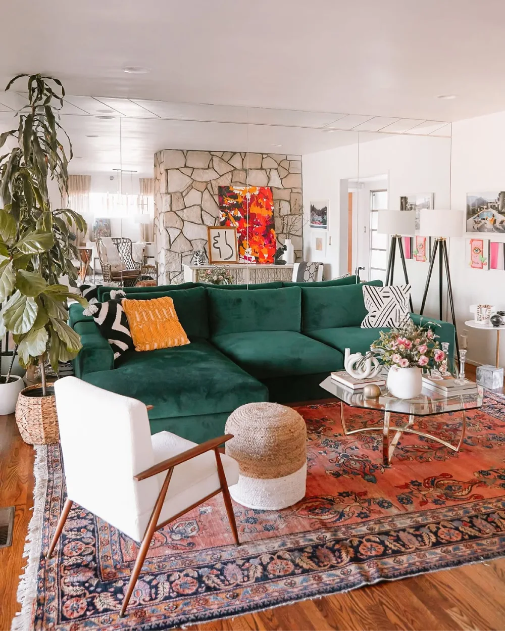 Deep green sectional with colorful pillows, an ornate rug, and a stone fireplace