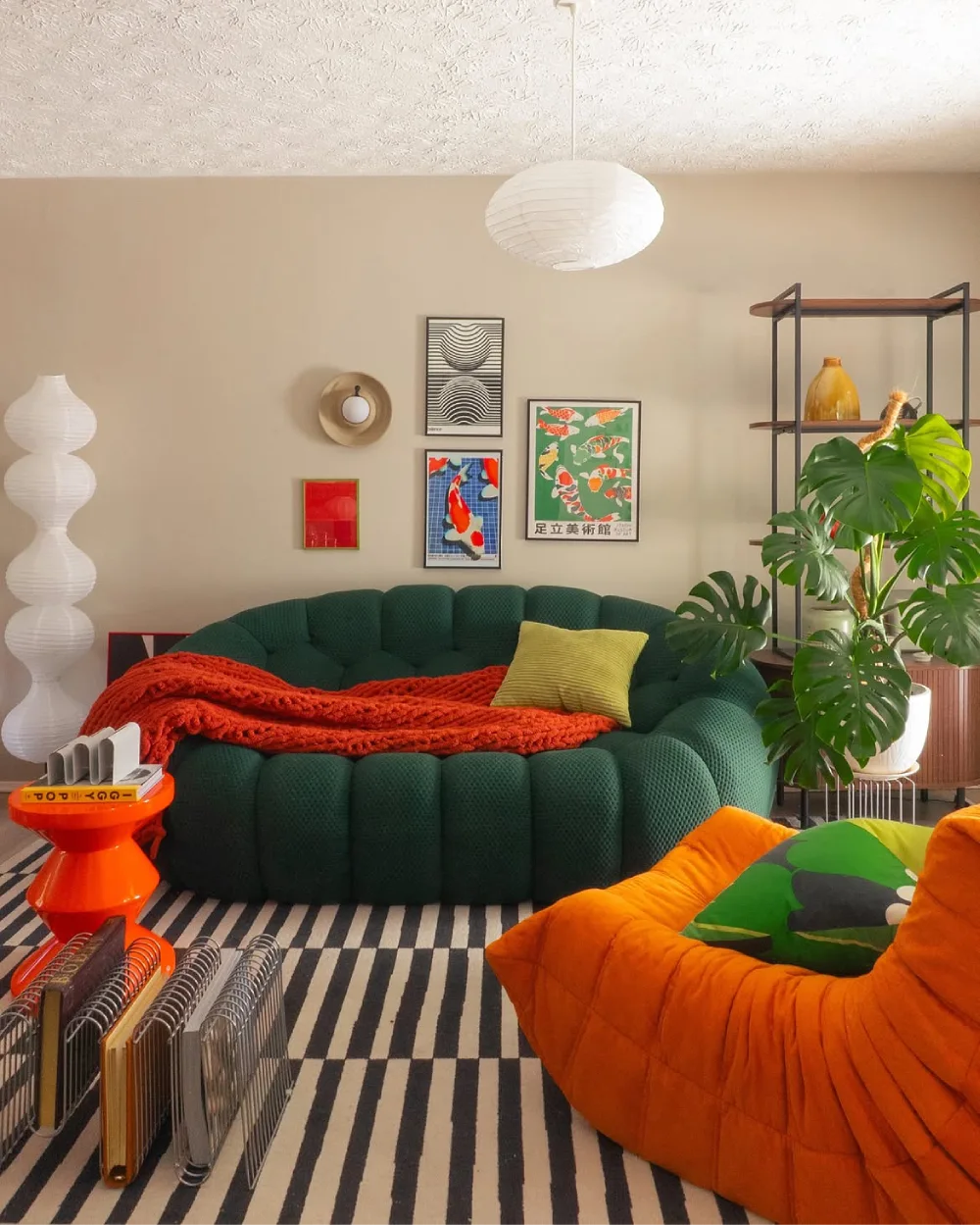 Deep green rounded sofa with orange furniture, colorful artwork, and striped rug