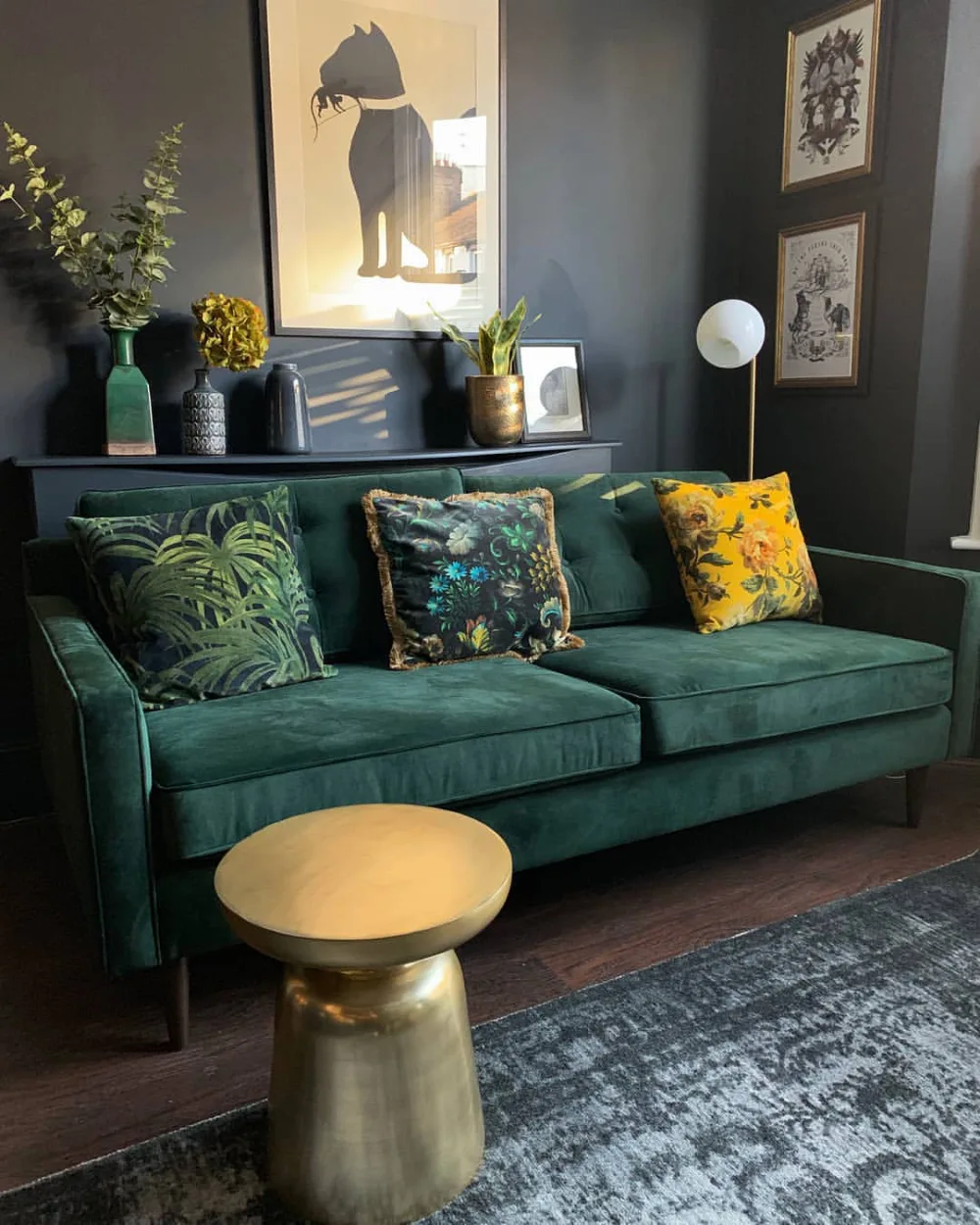 Deep green sofa with botanical pillows and gold accents in a dark living room