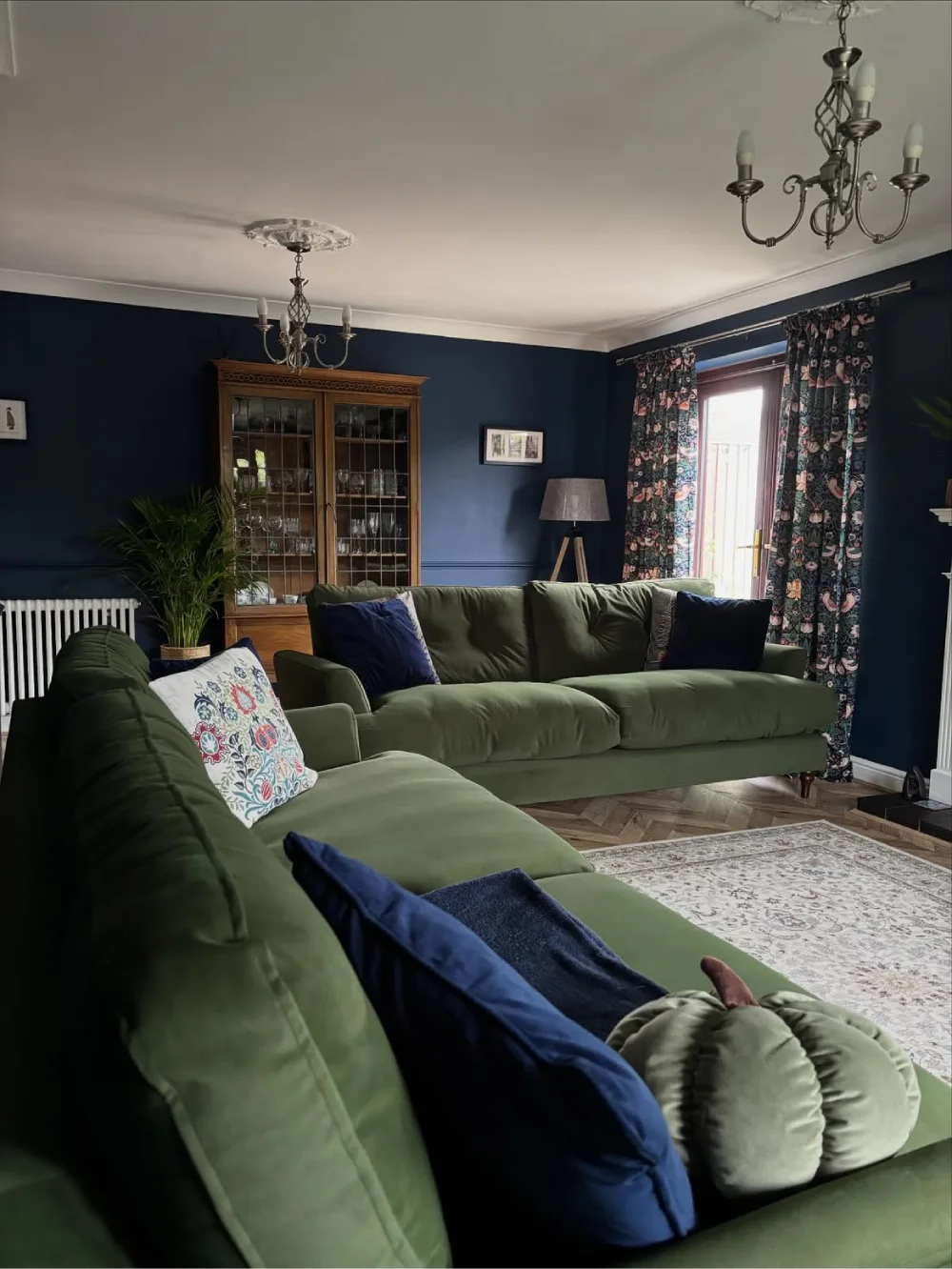 Forest green sectional sofa with navy walls and patterned curtains