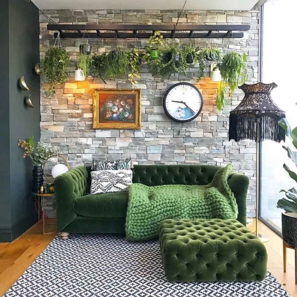 Dark green tufted sofa with green throw and ottoman against a stone wall