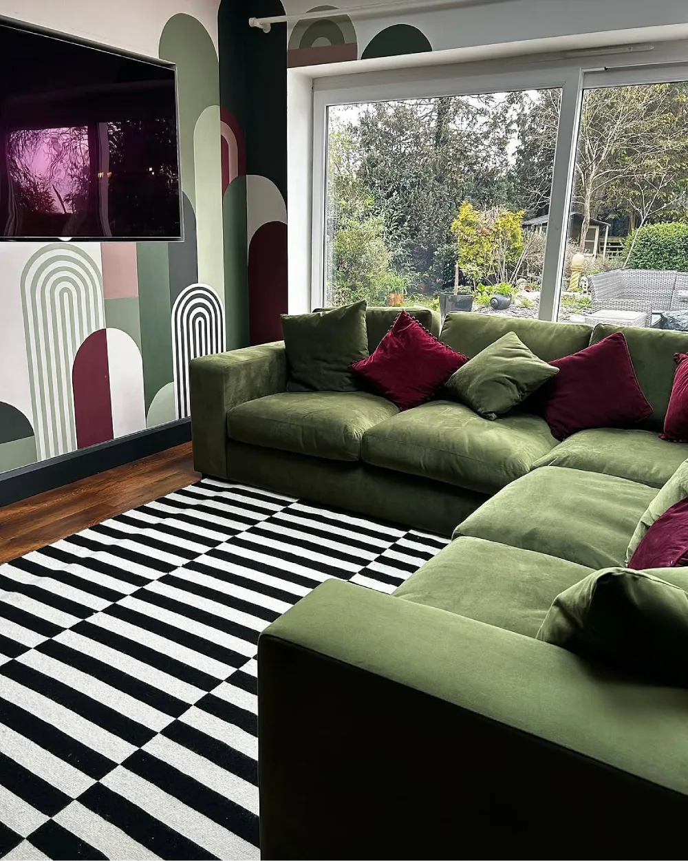 Olive green sectional with burgundy pillows and a black and white striped rug