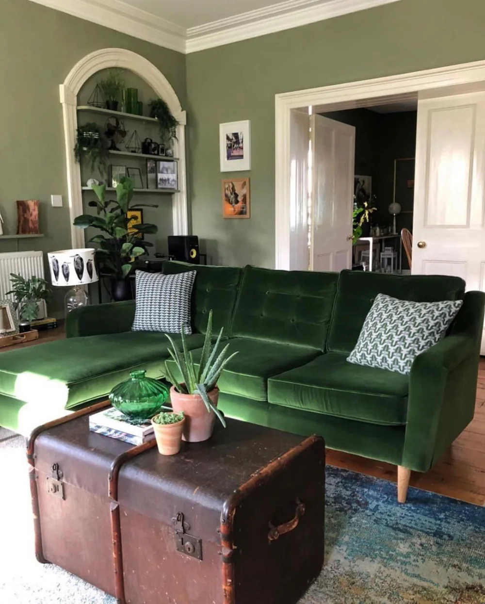 Dark green velvet sofa with vintage trunk coffee table and patterned pillows