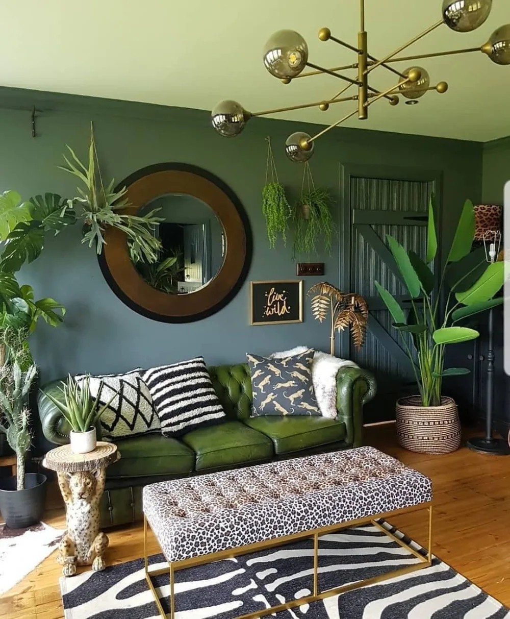 Green velvet sofa in a dark green living room filled with plants and patterned decor