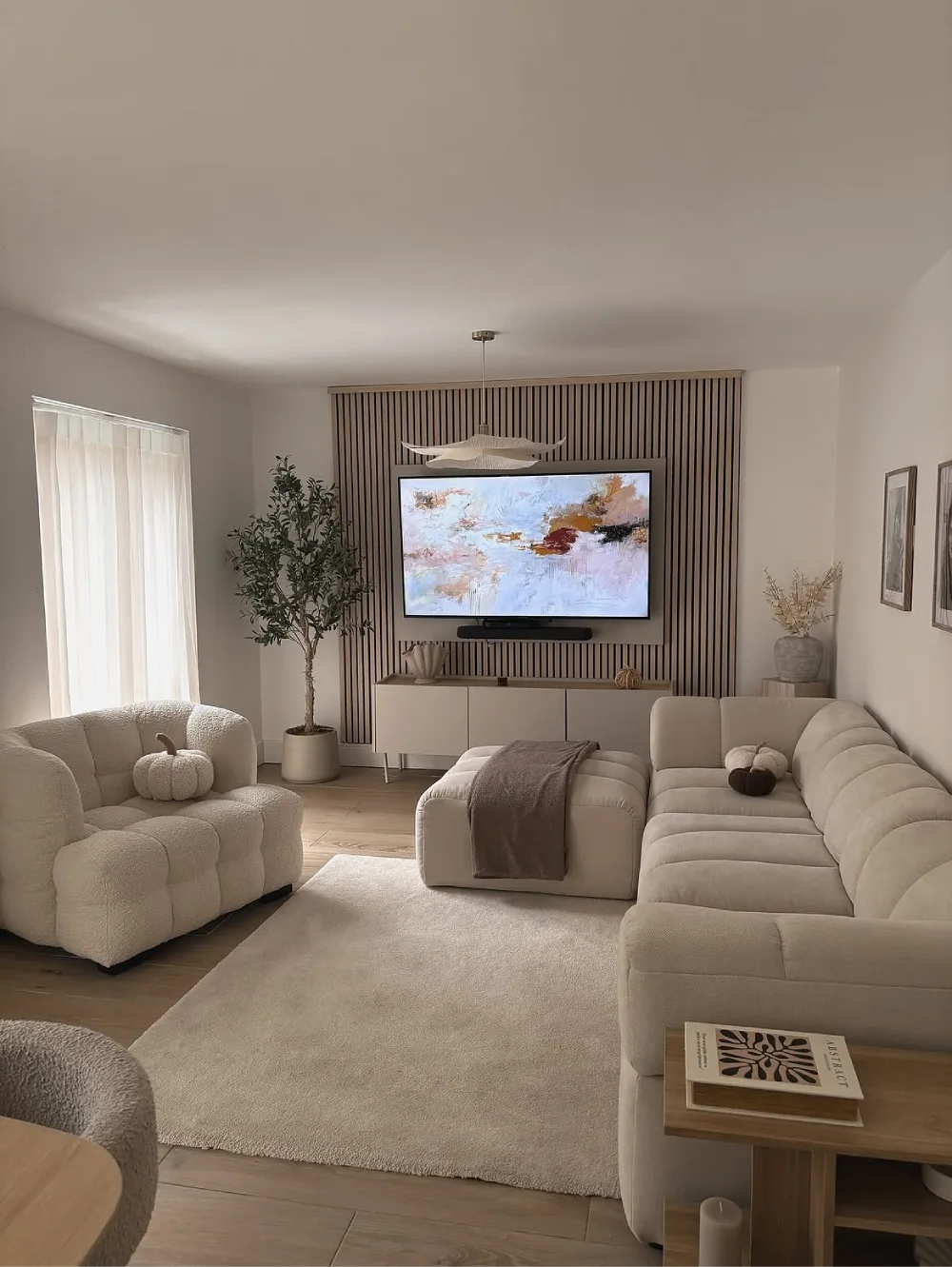 minimal neutral living room with curved cream seating, wood accents, and slatted TV wall