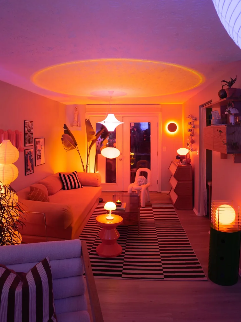 colorful living room with orange ambient lighting, striped rug, plants, and modern furniture